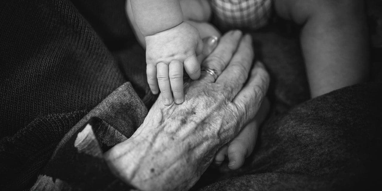 grayed closeup photo of old woman's hand and baby's hand