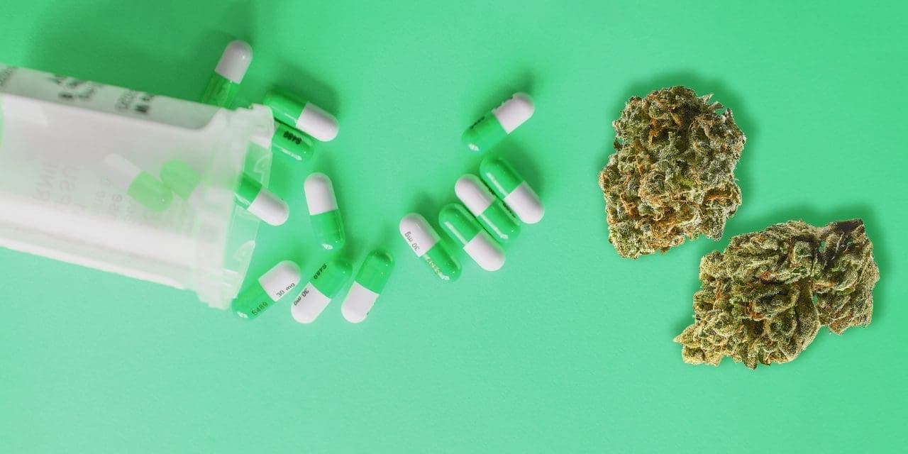 tumble down cup spilling green pills beside 2 cannabis buds